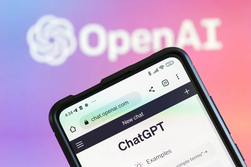 یک صفحه گوشی هوشمند رابط ChatGPT از OpenAI را با لوگوی OpenAI تار در پس‌زمینه رنگارنگ نمایش می‌دهد.