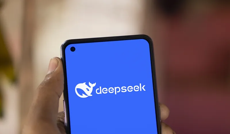یک تلفن دستی با آرم Deepseek و نماد نهنگ که در صفحه آبی روشن نشان داده شده است.