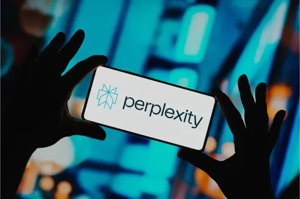 آرم آزمایشگاه های Perplexity که در تلفن های هوشمند نشان داده شده در دستان پس زمینه چراغ شهر آبی نشان داده شده است.